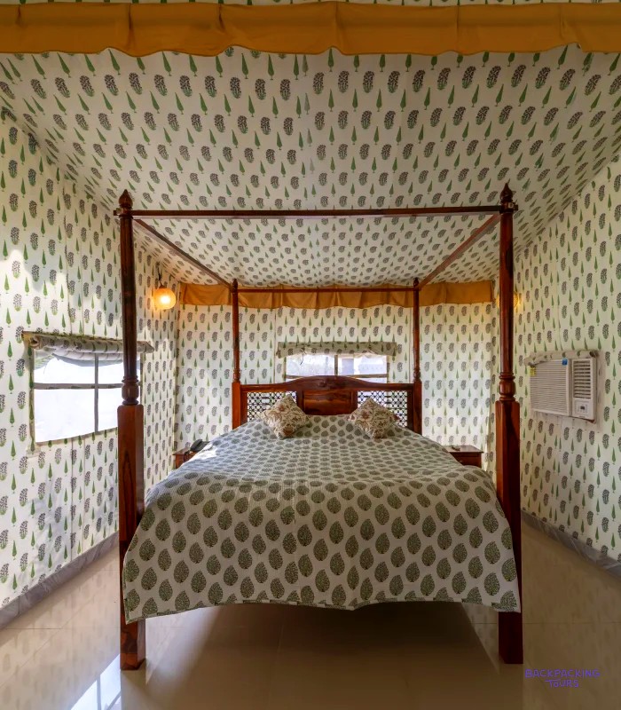 Inside a glamping tent, a four-poster bed with patterned bedding and printed fabric walls.