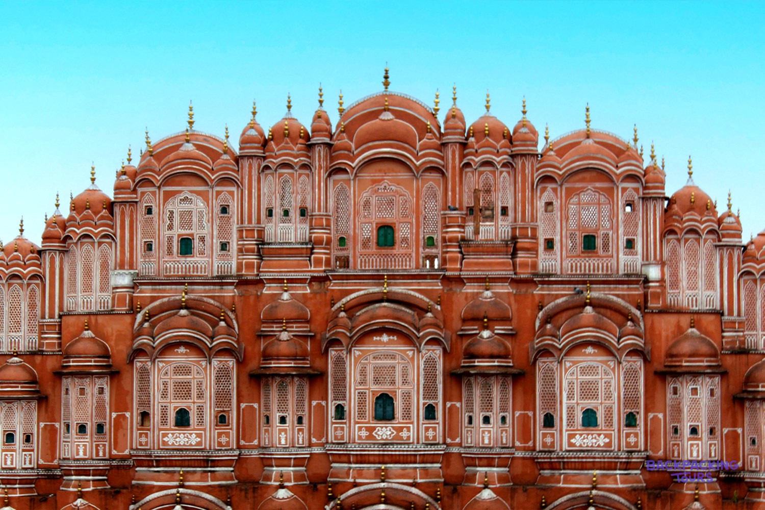 A grand, red-orange palace with many small, intricately carved windows and domed rooftops.
