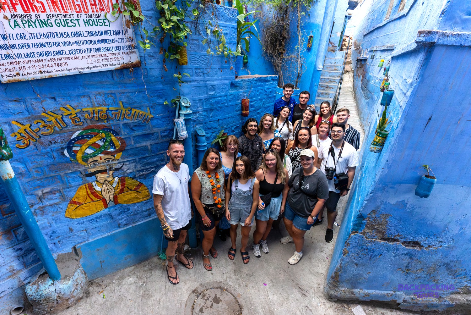 A group of travellers stands smiling in a narrow, vibrant blue alleyway with painted walls.