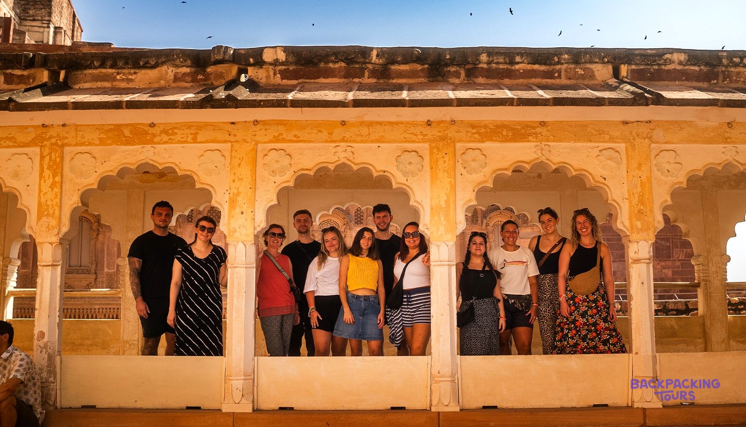 A group of people smiling and posing for a photo within an old, yellow-coloured building with ornate arches.