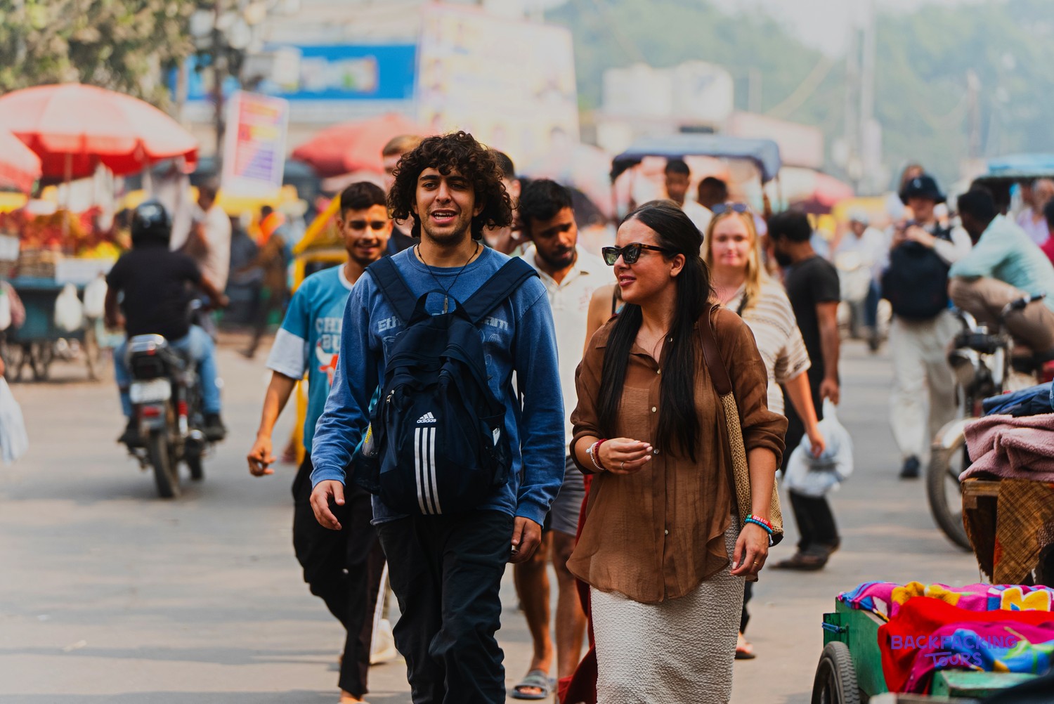 A man and a woman walk through a bustling street market, surrounded by other people and vehicles.