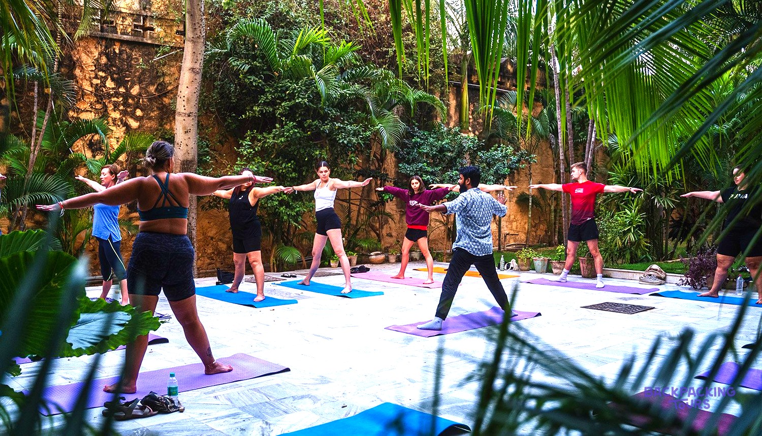 A group of people practise yoga outdoors on colourful mats in a lush green garden.