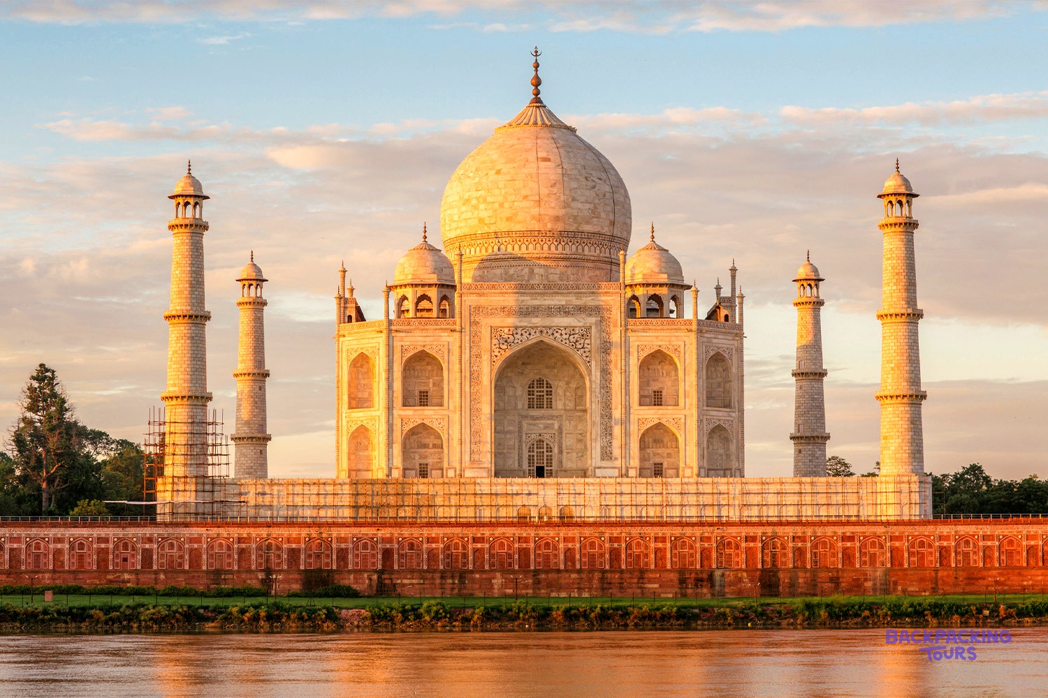 A grand white marble mausoleum with a large dome and four minarets glows at sunrise over water.