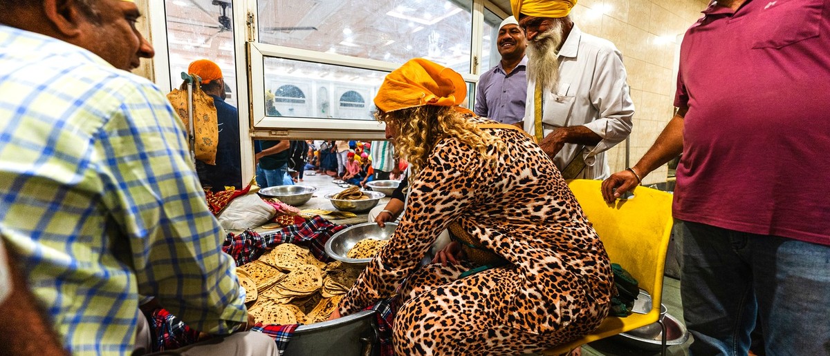 People, some in turbans, gather around flatbreads in a large container, with one woman serving.