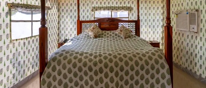 Inside a glamping tent, a four-poster bed with patterned bedding and printed fabric walls.