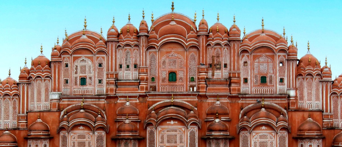 A grand, red-orange palace with many small, intricately carved windows and domed rooftops.