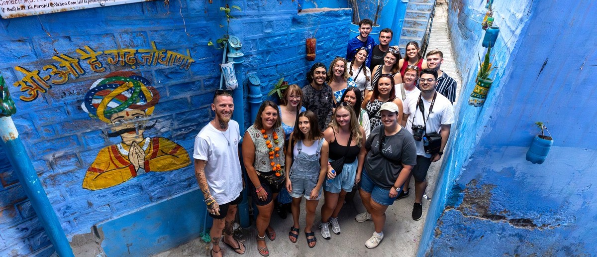 A group of travellers stands smiling in a narrow, vibrant blue alleyway with painted walls.