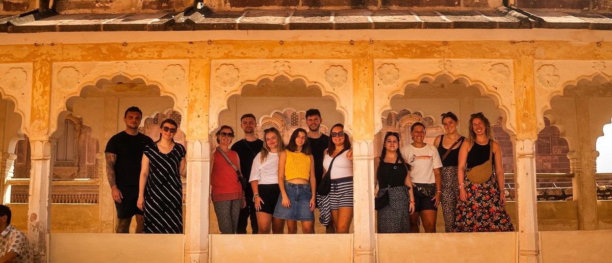 A group of people smiling and posing for a photo within an old, yellow-coloured building with ornate arches.