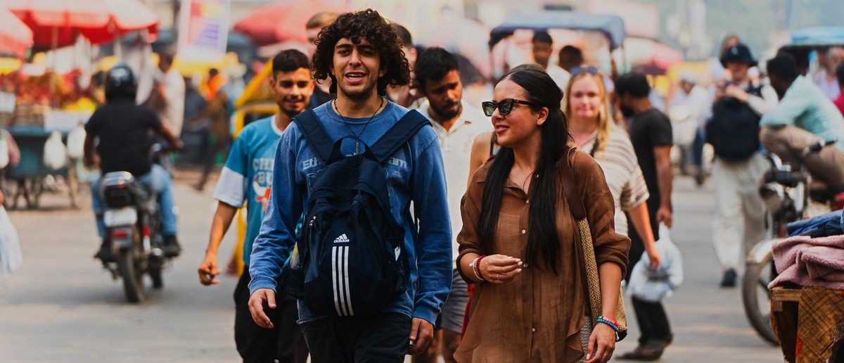 A man and a woman walk through a bustling street market, surrounded by other people and vehicles.