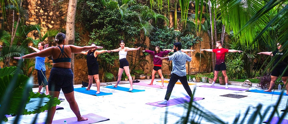 A group of people practise yoga outdoors on colourful mats in a lush green garden.