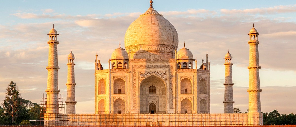 A grand white marble mausoleum with a large dome and four minarets glows at sunrise over water.