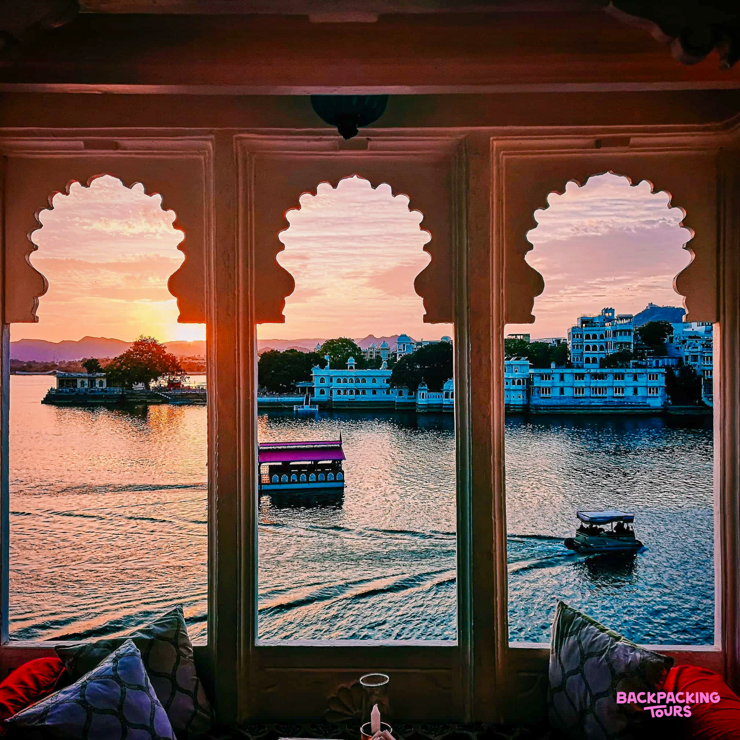 A serene sunset view over Lake Pichola in Udaipur, with boats cruising past historic palaces.