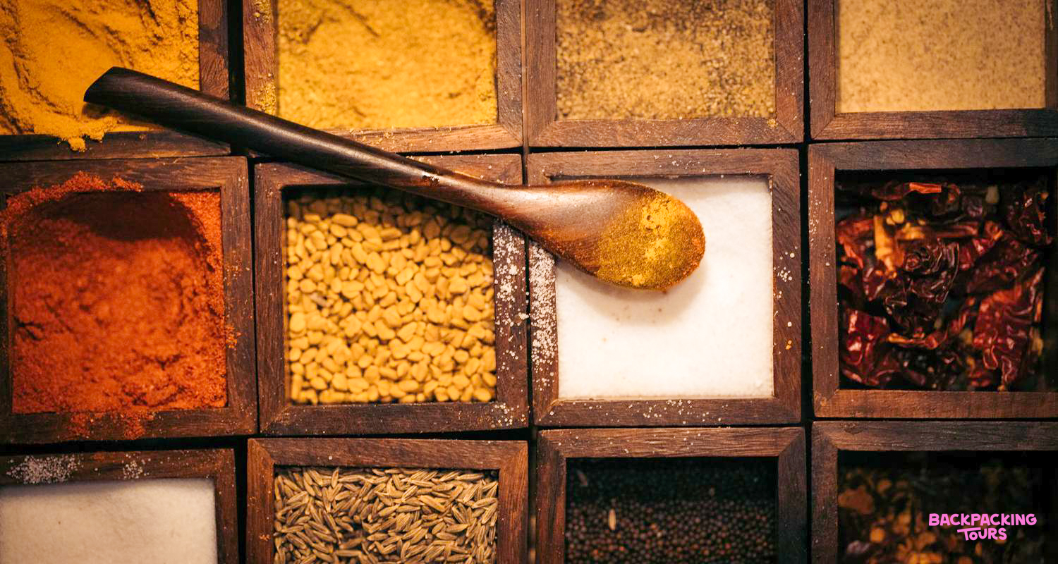 A wooden spoon rests on a vibrant array of Indian spices in a cooking class in Udaipur.