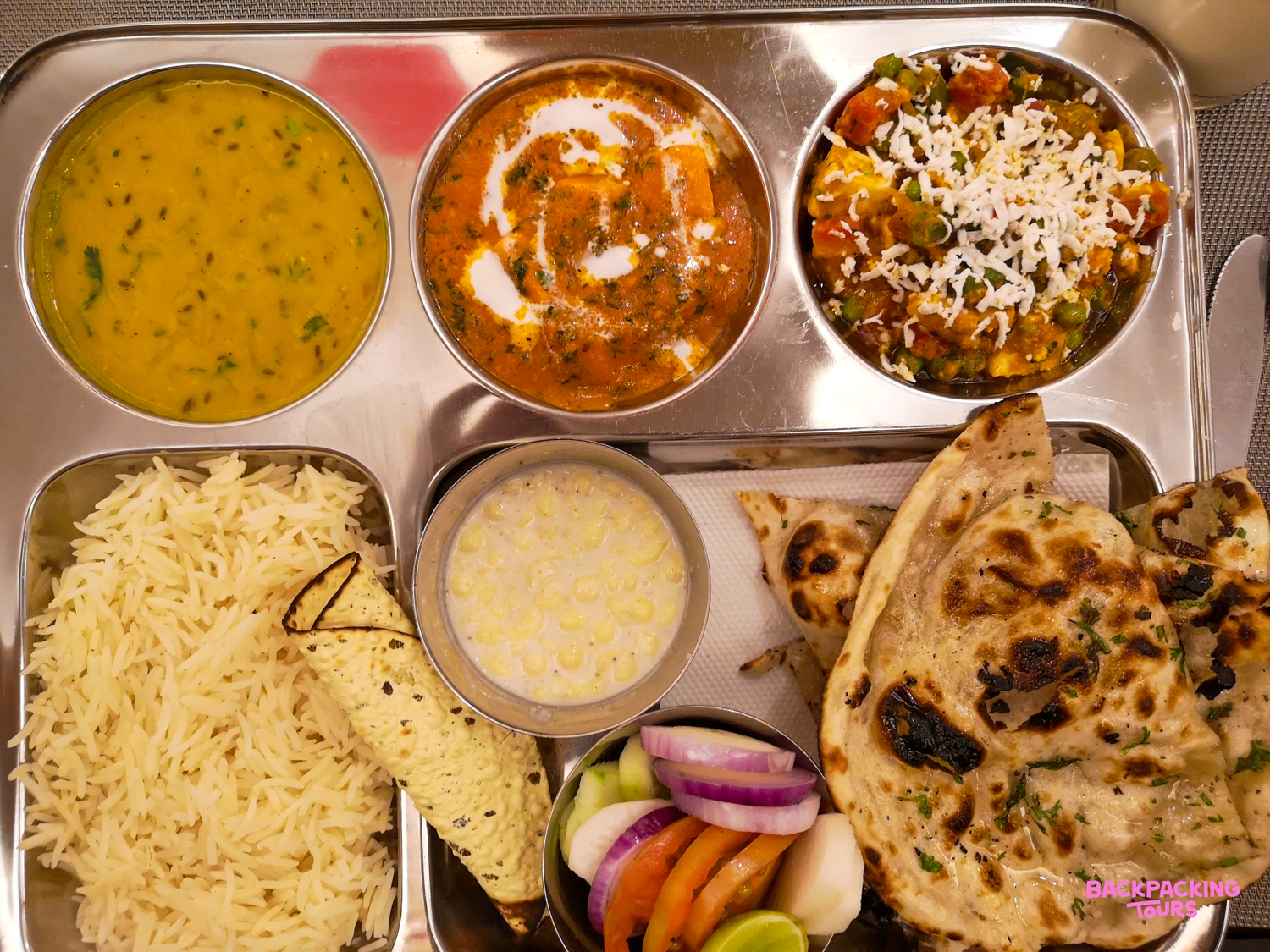 A mouth-watering North Indian thali meal, including paneer, dal, rice, naan, raita, and fresh salad.