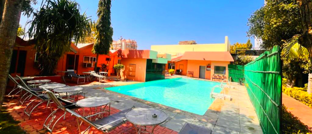 Relaxing swimming pool area with colorful buildings and sun loungers under a clear sky in Pushkar.
