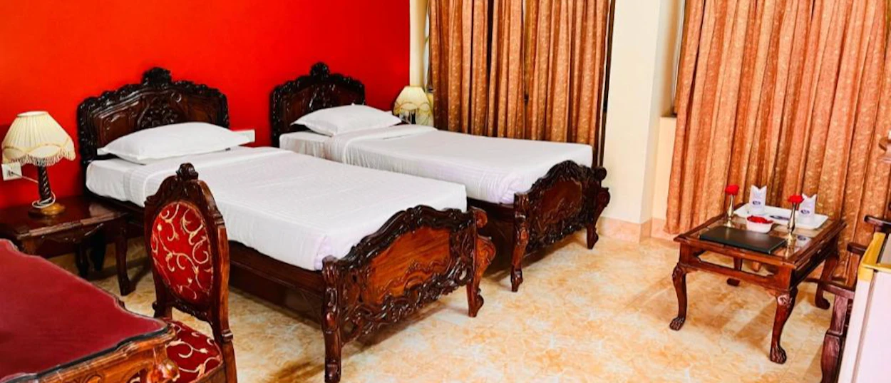 A cozy hotel room featuring two single beds, red walls, and traditional wooden furniture.