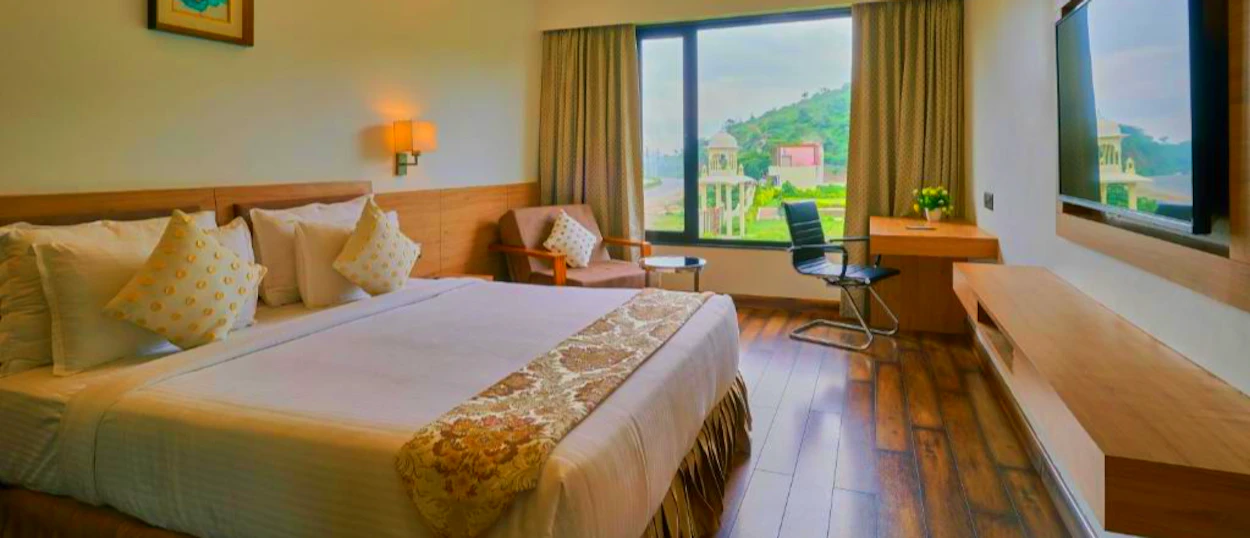 Comfortable hotel room in Udaipur with a scenic view of green hills and white structures.