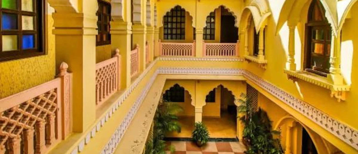 An ornate yellow courtyard with arched windows and intricate pink railings in Jaipur, India.