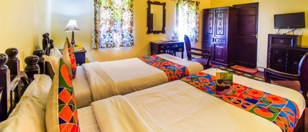 A vibrant hotel room in Jaipur with two beds, colorful patterned textiles, and dark wooden furniture.