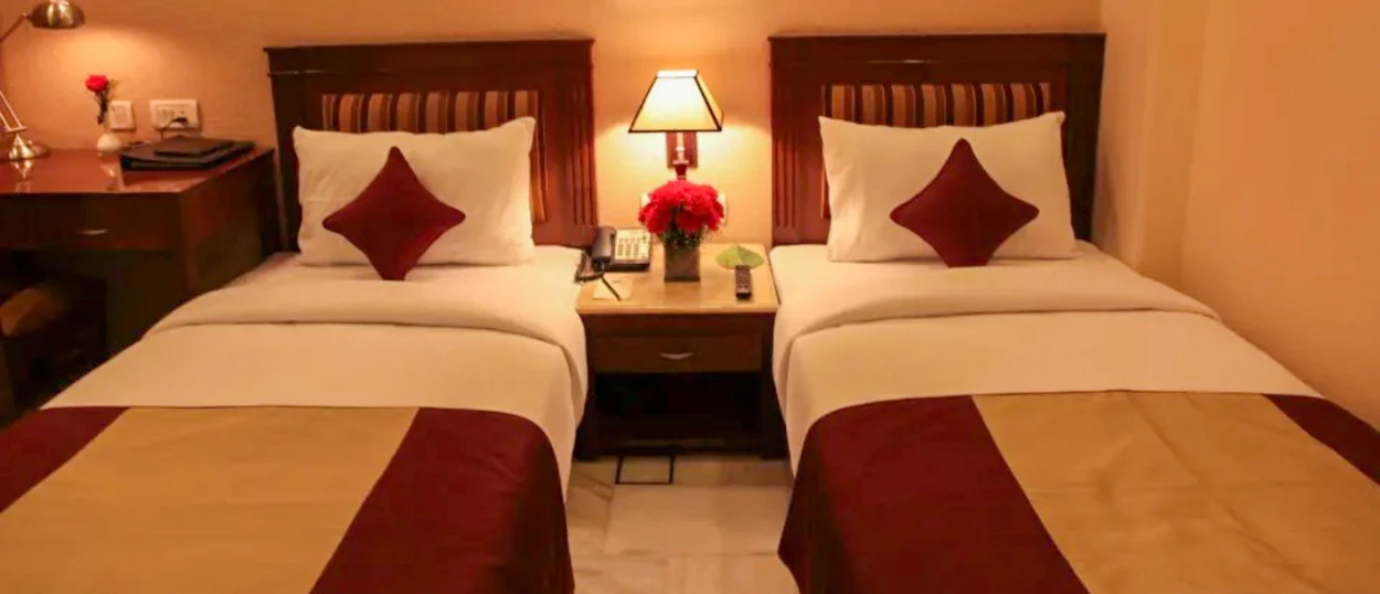 A comfortable hotel room in New Delhi with two single beds and warm lighting.