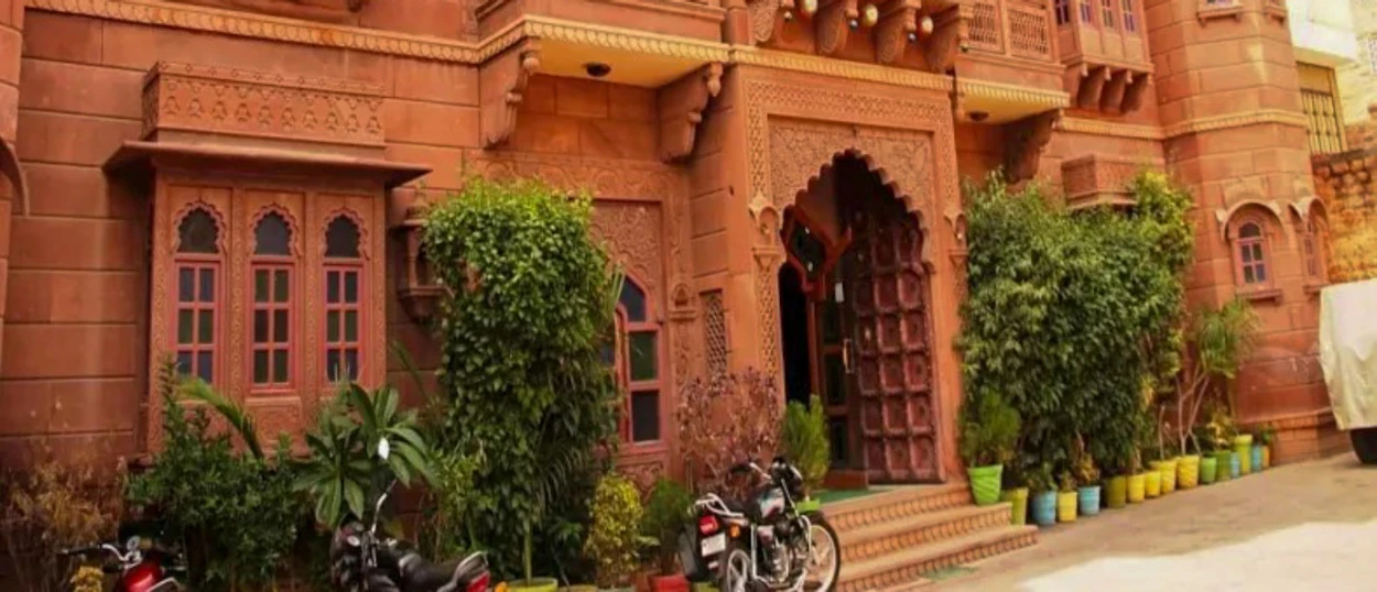 A traditional red sandstone haveli in Jodhpur, India, with intricate carvings and parked motorcycles.
