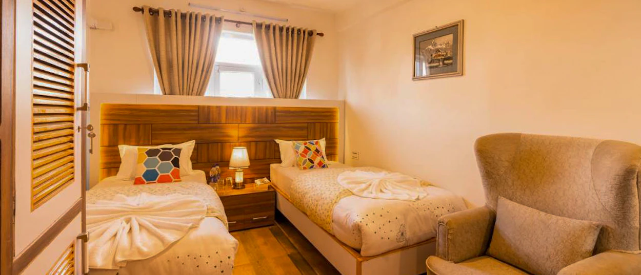 A comfortable hotel room with two single beds, a bedside lamp, and an armchair in Kathmandu.