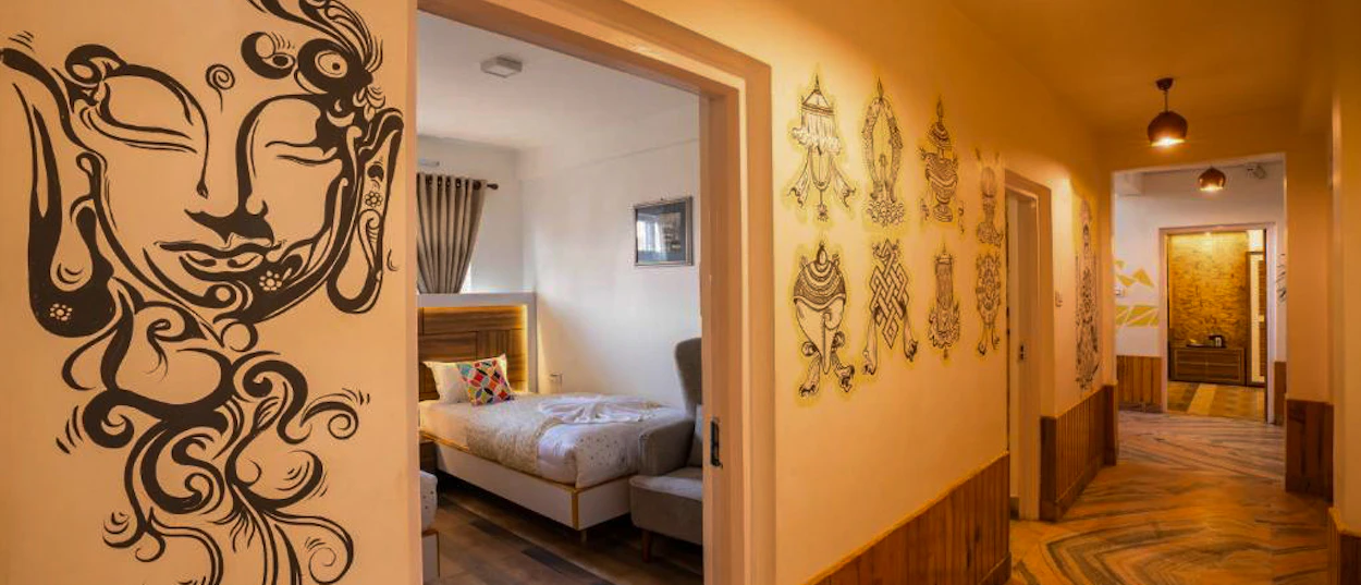 A warm hallway with a Buddha mural and traditional art, leading to a cozy room in Kathmandu.