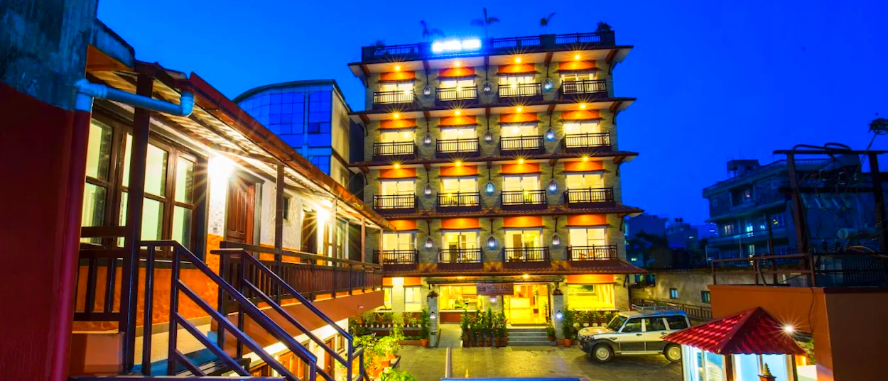 A multi-story hotel with warmly lit rooms and traditional balconies at twilight in Pokhara.