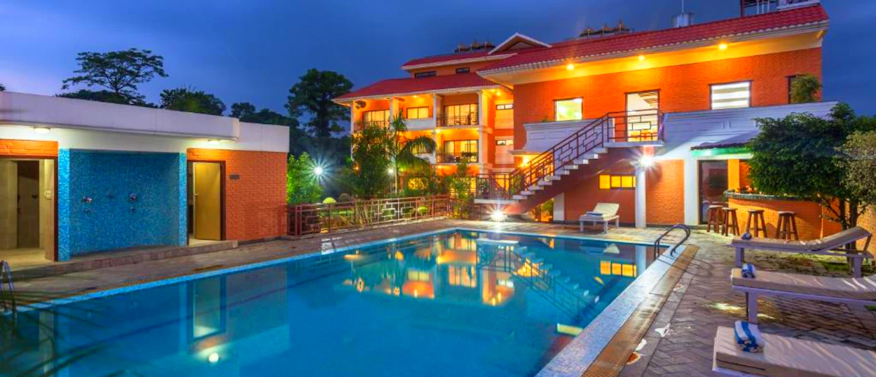 An inviting lodge with a sparkling swimming pool and warm lights at dusk in Chitwan National Park.