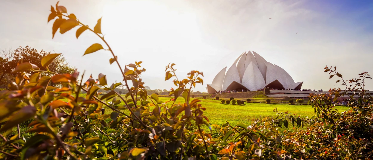The stunning white Lotus Temple rises above green lawns and sun-drenched bushes in New Delhi.