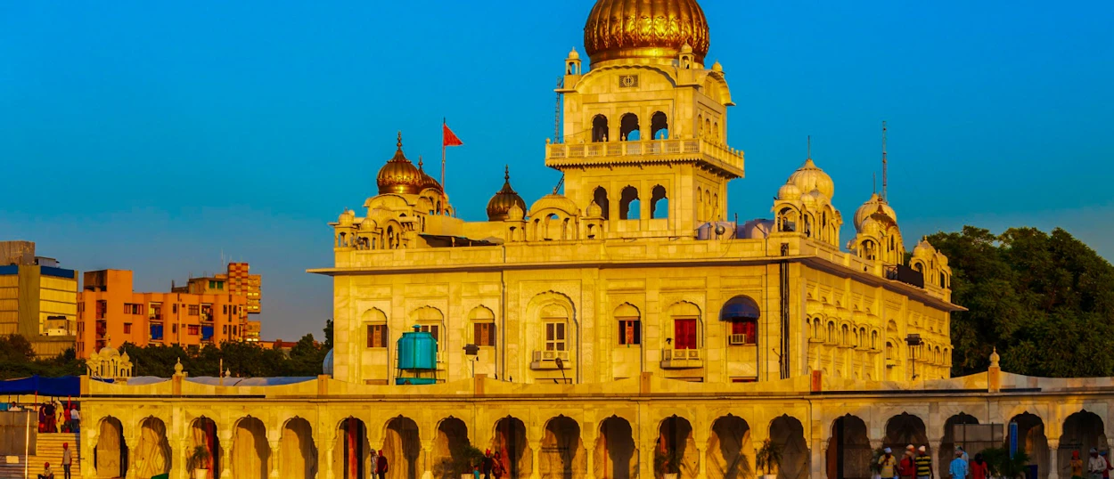 A majestic golden-domed Sikh temple in Delhi, featuring ornate architecture under a clear blue sky.