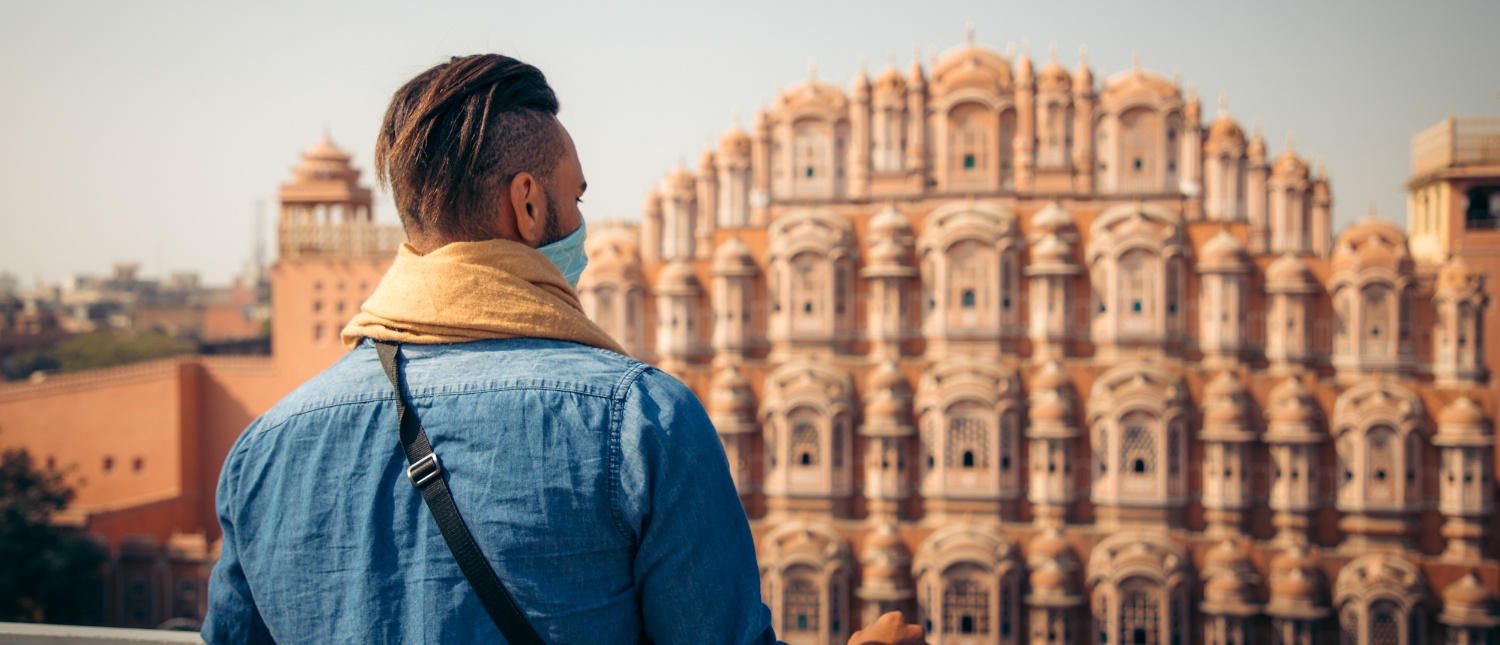 A masked traveler admires the beautiful Hawa Mahal palace, a landmark of Jaipur's Pink City.