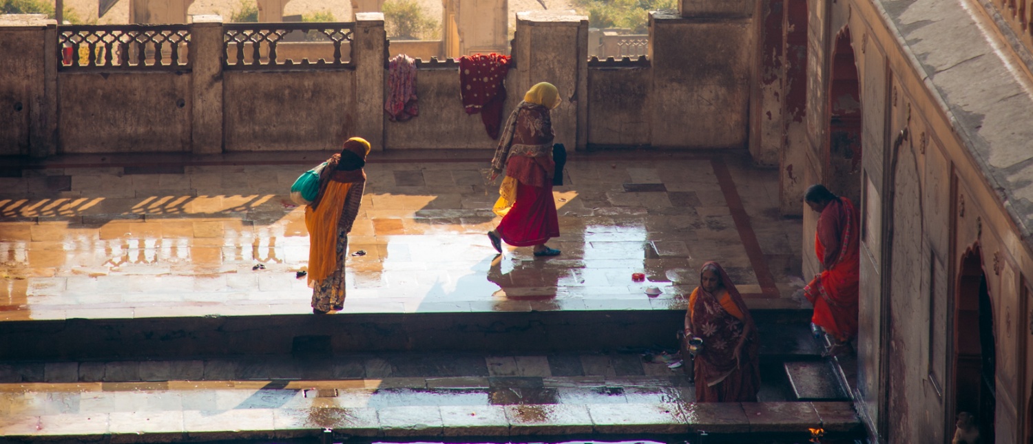 Vibrantly dressed women walk through a sunlit palace courtyard in Jaipur, India.