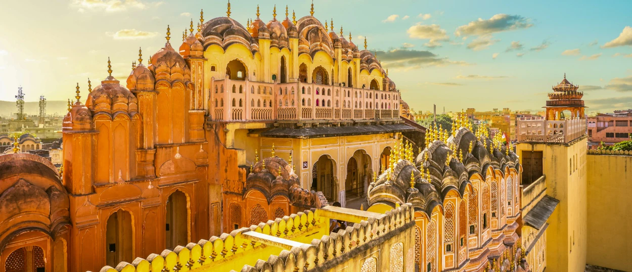 The ornate Hawa Mahal palace in Jaipur, India, glows pink and yellow under a bright sky.