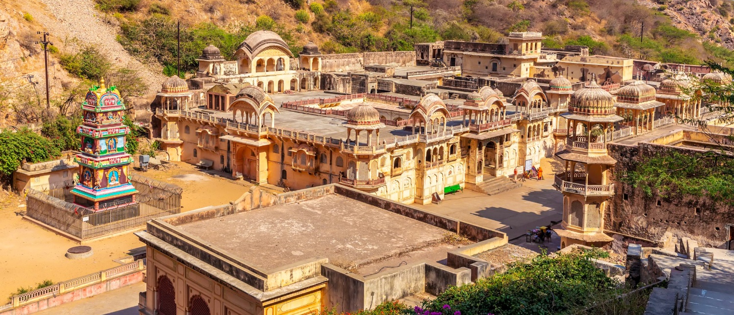 Historic stone temples and buildings with domes and a colorful shrine in the hills of Jaipur.
