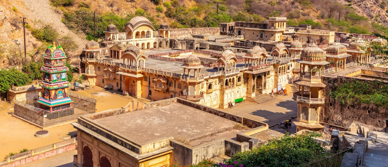 Historic stone temples and buildings with domes and a colorful shrine in the hills of Jaipur.