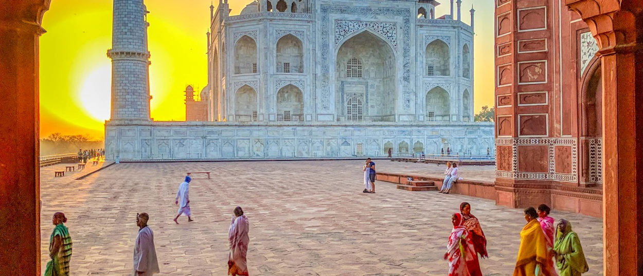 Tourists explore the majestic Taj Mahal in Agra at sunrise, framed by red sandstone arches.