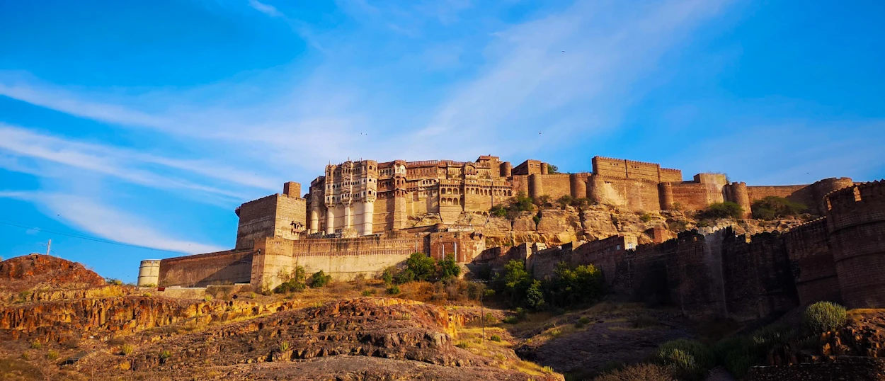 The imposing Mehrangarh Fort in Jodhpur rises from rocky hills against a vibrant blue sky.