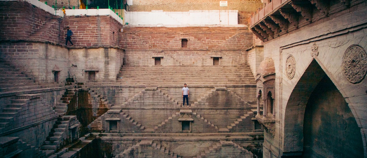 A lone traveler stands amidst the geometric steps of a magnificent ancient stepwell in Jodhpur.