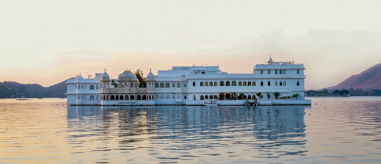 Elegant white palace on Lake Pichola, Udaipur, reflecting in calm water at sunset.