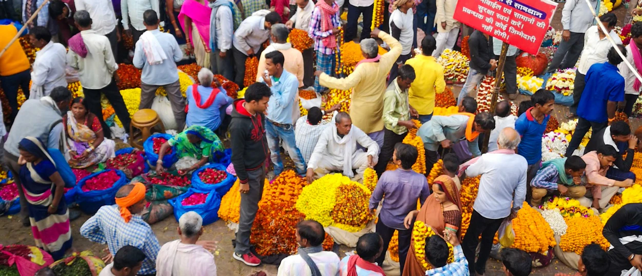 Crowded flower market in Udaipur with people sorting and selling colorful garlands and loose blossoms.