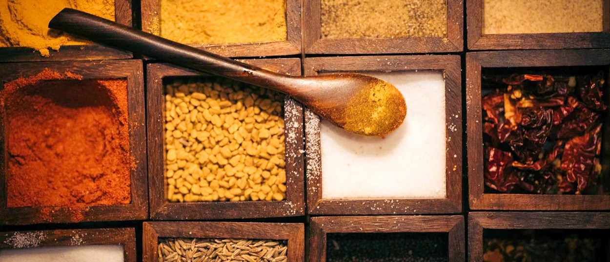 A wooden spoon filled with yellow spice rests on a box of colorful Indian spices.