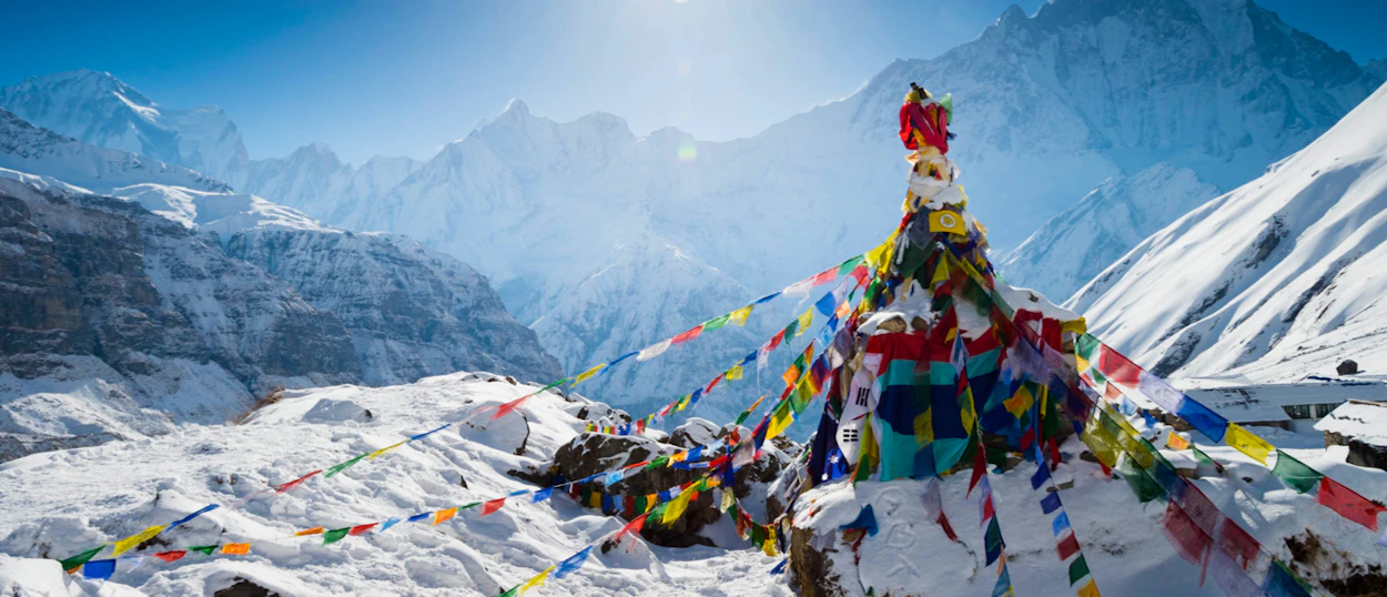 Vibrant prayer flags on a snowy peak overlooking the majestic Annapurna Mountain Range in Nepal.
