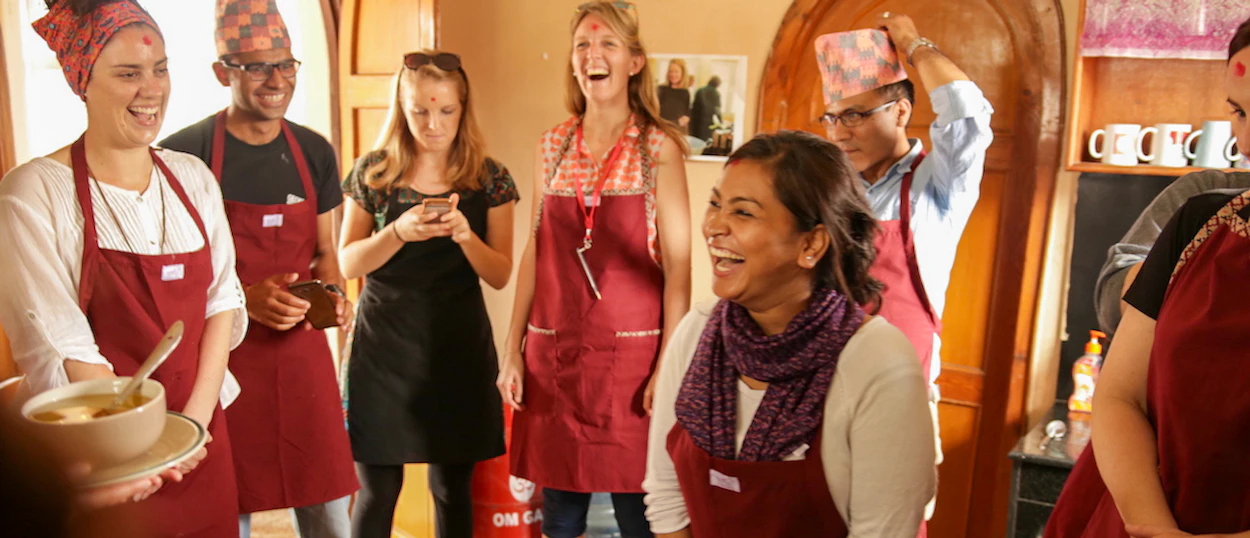Happy group of people in aprons laughing during a cooking class in Kathmandu.