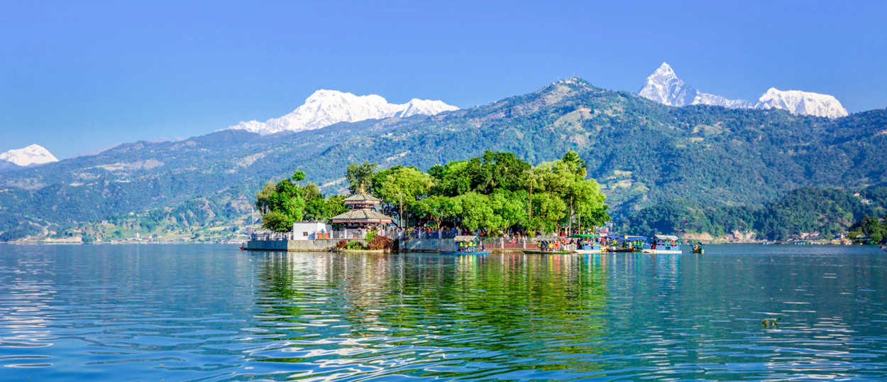 Serene Phewa Lake in Pokhara with Tal Barahi Temple on an island and towering Himalayas.