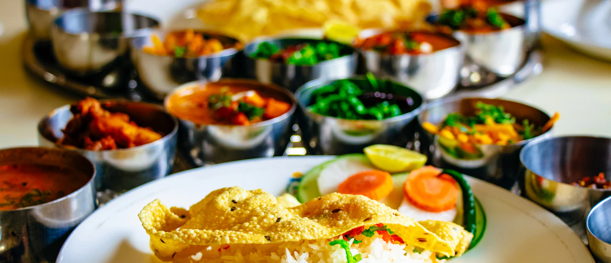 A vibrant Nepali thali meal featuring various curries, rice, papadum, and fresh vegetables.