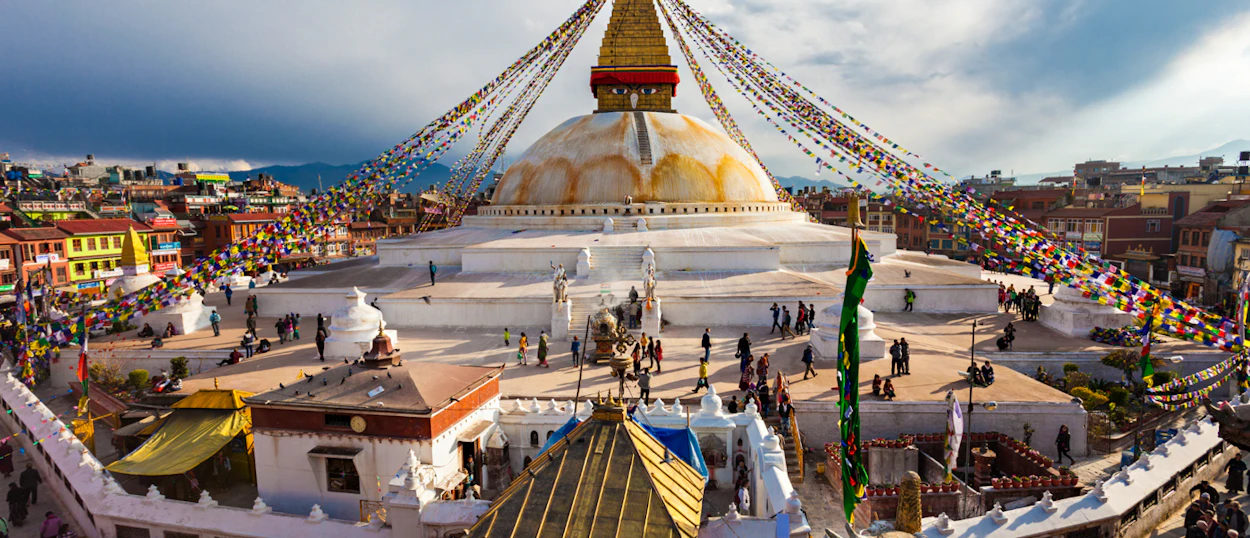 Visitors explore the serene Swoyambhunath Stupa in Kathmandu, surrounded by colorful buildings and prayer flags.