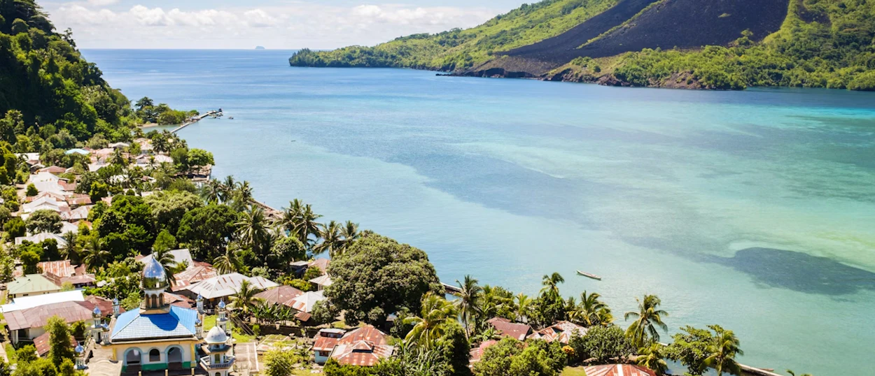 Tropical coastal town in Padang, Indonesia, with a mosque, houses, and calm turquoise sea.