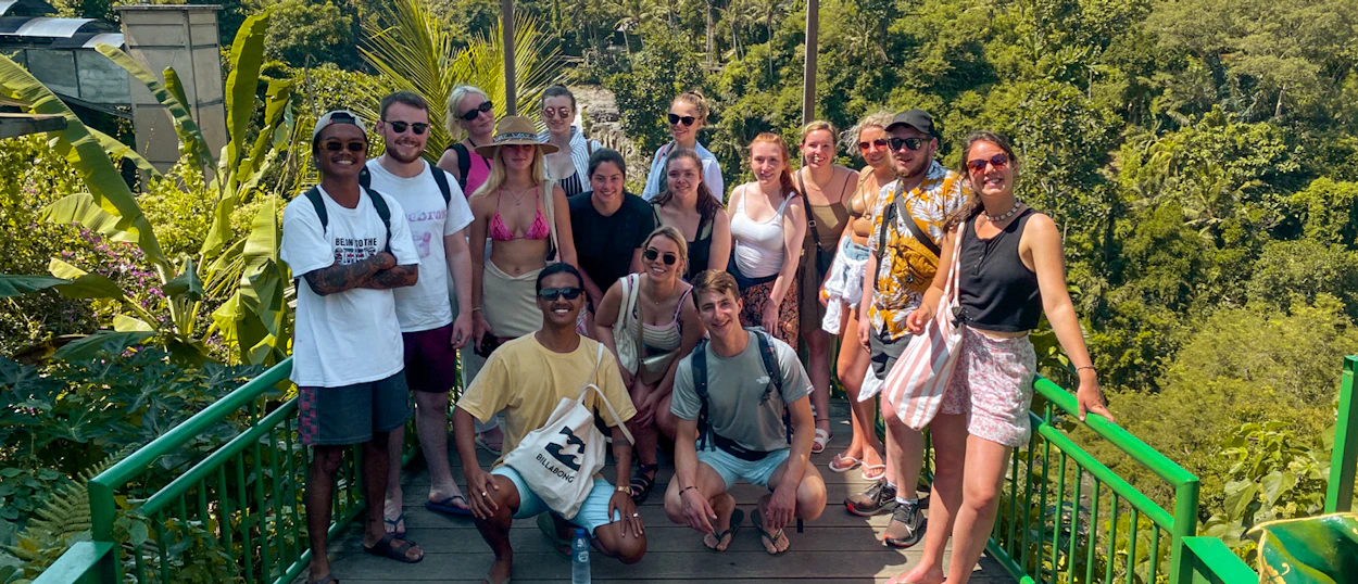 A happy group of backpackers posing on a bridge overlooking the lush Ubud jungle.
