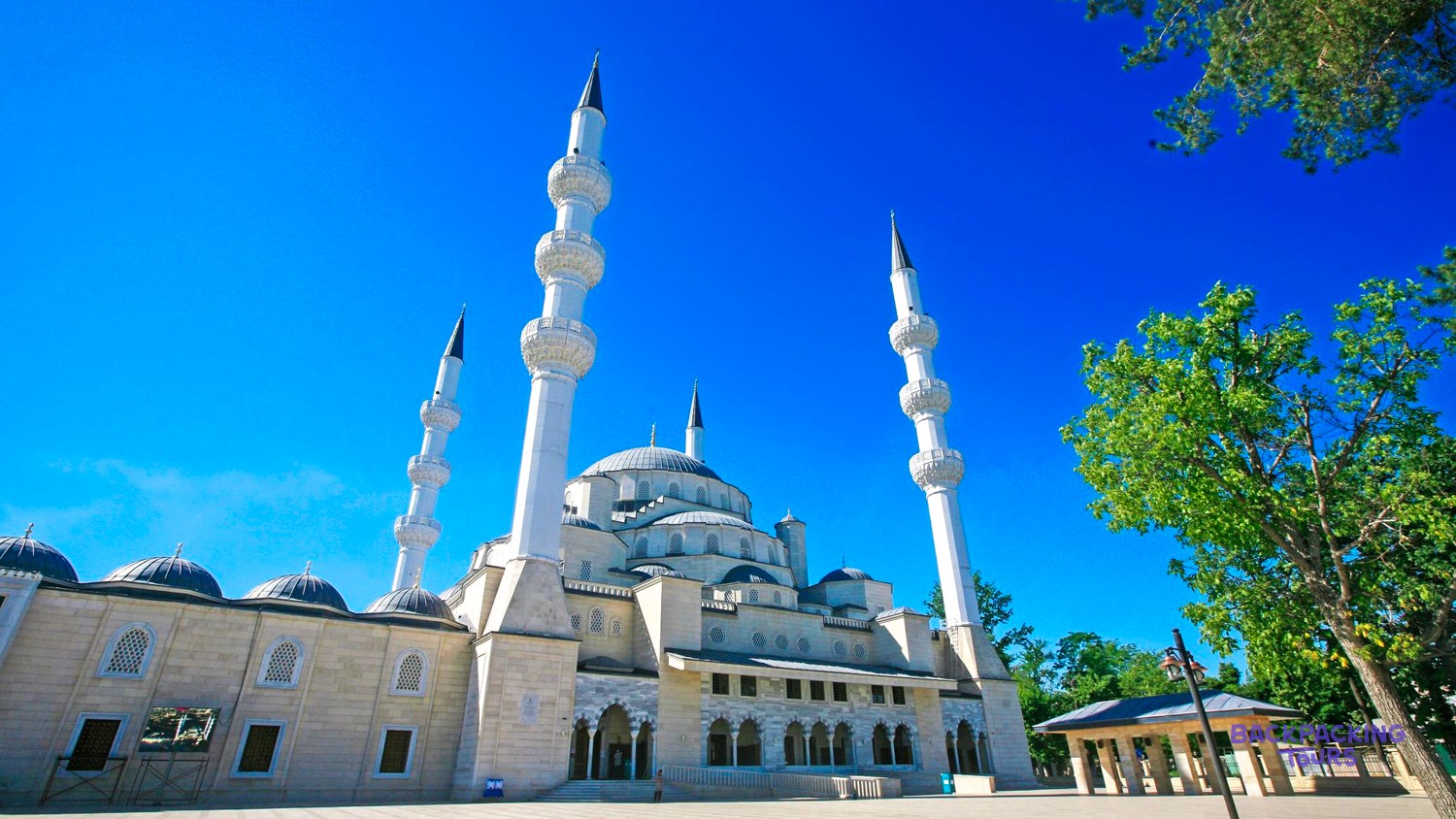 A grand mosque with multiple domes and four tall minarets stands under a bright blue sky.